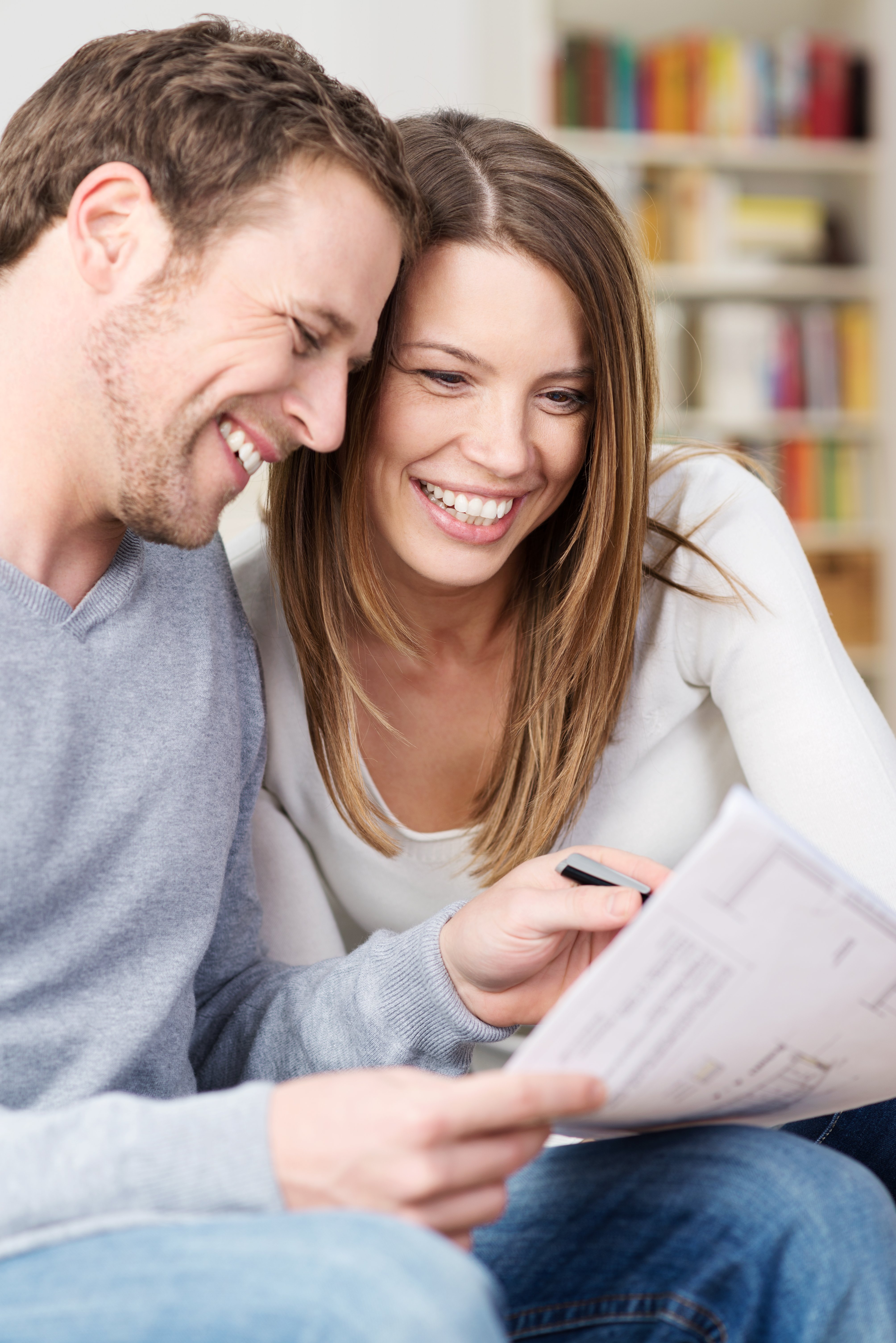 Close up portrait of an attractive young couple laughing as they discuss paperwork together at home in the living room