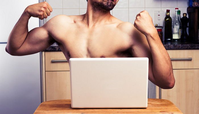Naked young man is flexing his muscles as he's engaging in a webcam chat on his laptop