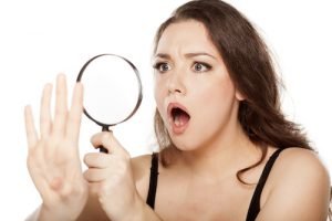 shocked young woman looking at her nails with a magnifying glass