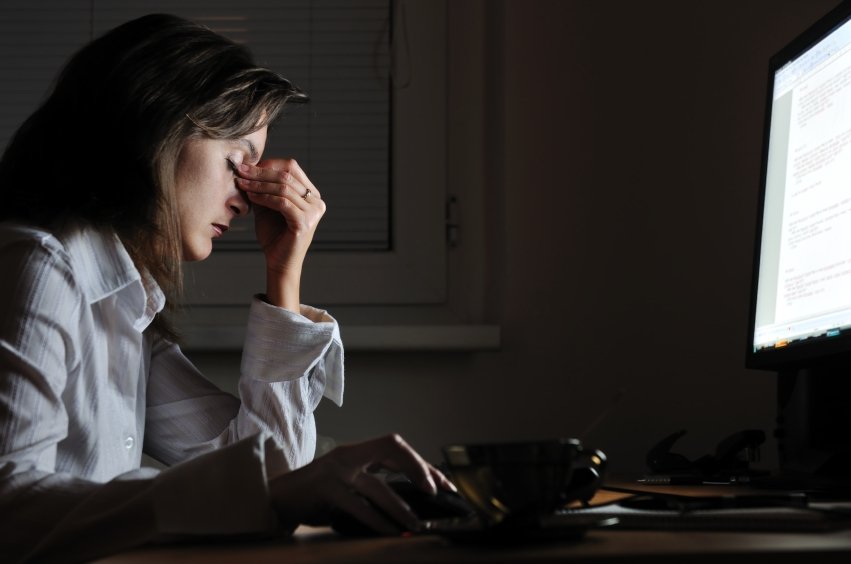 Young tired business woman with headache sitting at computer in workplace - night overtime work