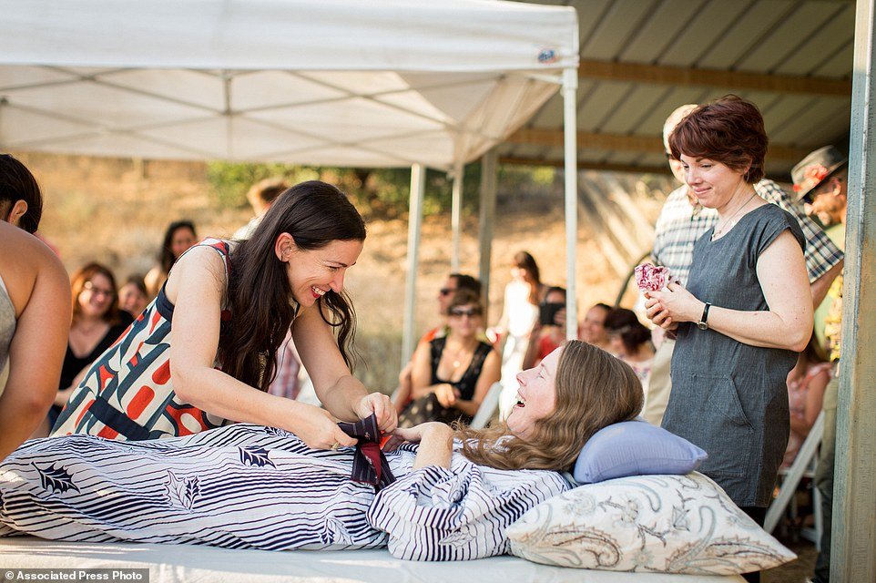 This July 24, 2016 photo provided by Niels Alpert, Amanda Friedland, left, surrounded by friends and family adjusts her friend Betsy Davis's sash as she lays on a bed during her "Right To Die Party" in Ojai, Calif. In early July, Davis emailed her closest friends and family to invite them to a two-day celebration, telling them: "These circumstances are unlike any party you have attended before, requiring emotional stamina, centeredness, and openness. And one rule: No crying." The 41-year-old woman diagnosed with ALS, held the party to say goodbye before becoming one of the first California residents to take life-ending drugs under a new law that gave such an option to the terminally ill. (Niels Alpert via AP)