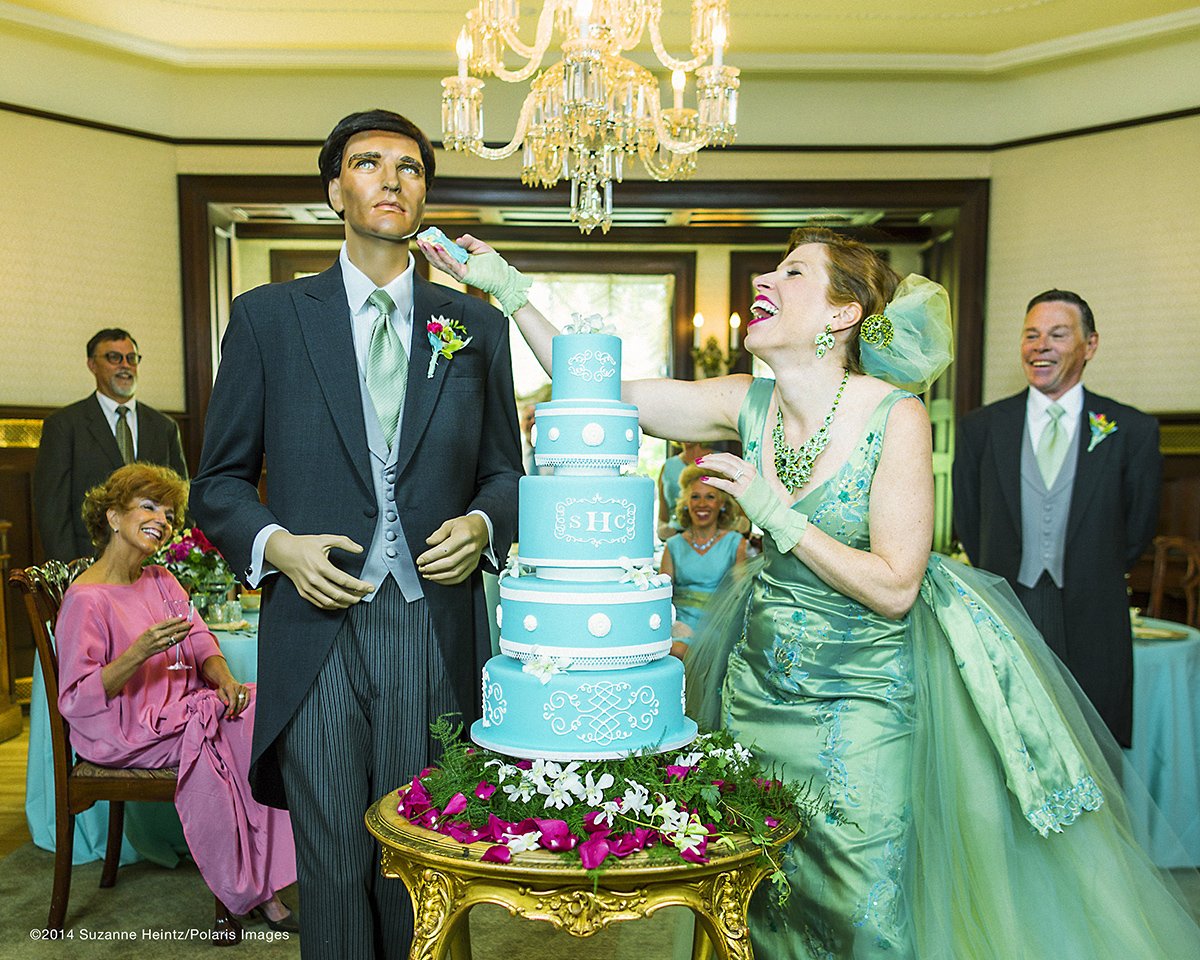 June 16, 2014 - Denver, Colorado, USA: American Conceptual Photographer, Suzanne Heintz, poses for a self portrait as she feeds her imitation husband a peice of cake after a satirical renewal of the vows ceremony. Part of her 14 year photo series, LIFE ONCE REMOVED, in which Heintz satirizes the image of a "Perfect Life." She uses humor to comment on mid-20th Century societal expectations still present for women of a "Certain Age" to marry and have children. She recreates all aspects of family life with her store bought husband and daughter, featuring them in scenes of blissful domestic life in and outside of the home, traditional holidays, and idyllic family vacations. (Suzanne Heintz / Polaris)