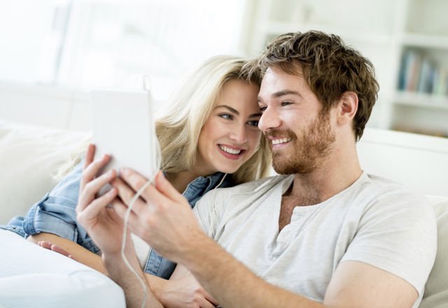 Happy young couple at home video chatting using app on a tablet computer