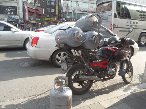 가스통을 가득 싣고 차도에 세워둔 오토바이가 위험하기 짝이 없고, 자칫 달리다 도로 바닥에 떨어뜨리기라도 한다면 엄청 난 화를 불러올 것이다.