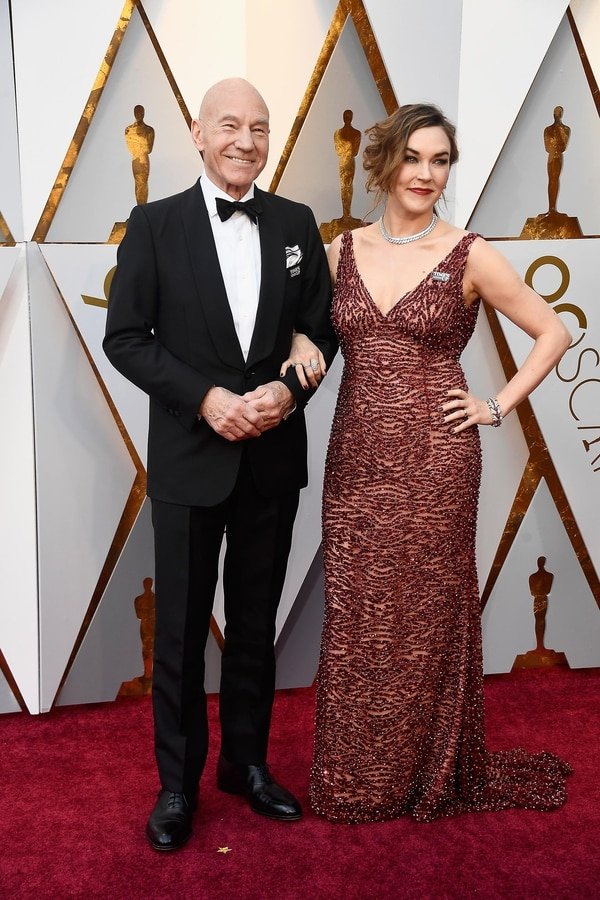 Patrick Stewar y Sunny Ozell se hicieron presentes en la gala de los Oscar. Él impecable black tie con moño de terciopelo y zapatos acordonados de cuero y su mujer lo acompañó con un vestido bordeaux escote V bordado. De joyas eligió pulsera, anillos, gargantilla y aros.