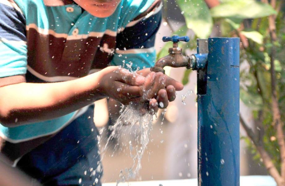 Un joven toma agua potable de la llave