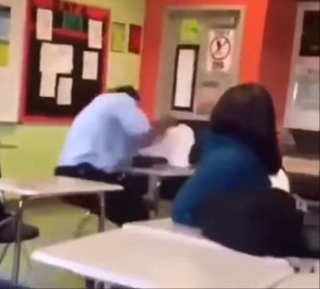 O aluno, de branco, é visto de lado batendo em cima da mesa após o corpo bater