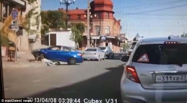 La voiture monte le trottoir et s'écrase dans un arbre tandis que la femme se lève de façon instable et tente de s'égarer dans la peur