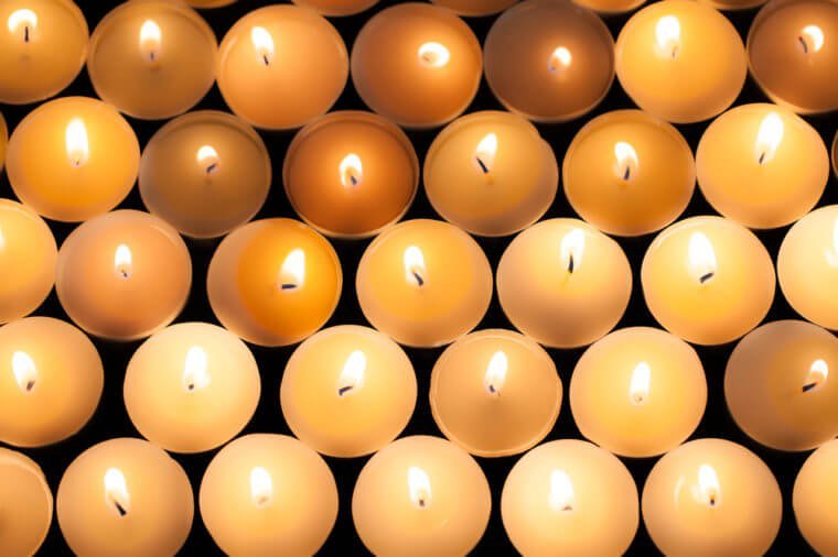 Lighted tealight candlelight background image. Lit flaming candles in rows from above. Backdrop of beautiful warm orange glow from wax candle flames. 