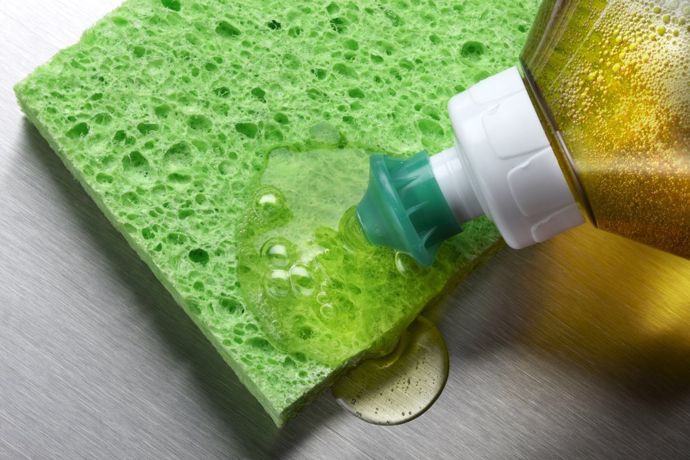 macro shot of dish soap being squeezed onto green sponge in aluminum sink