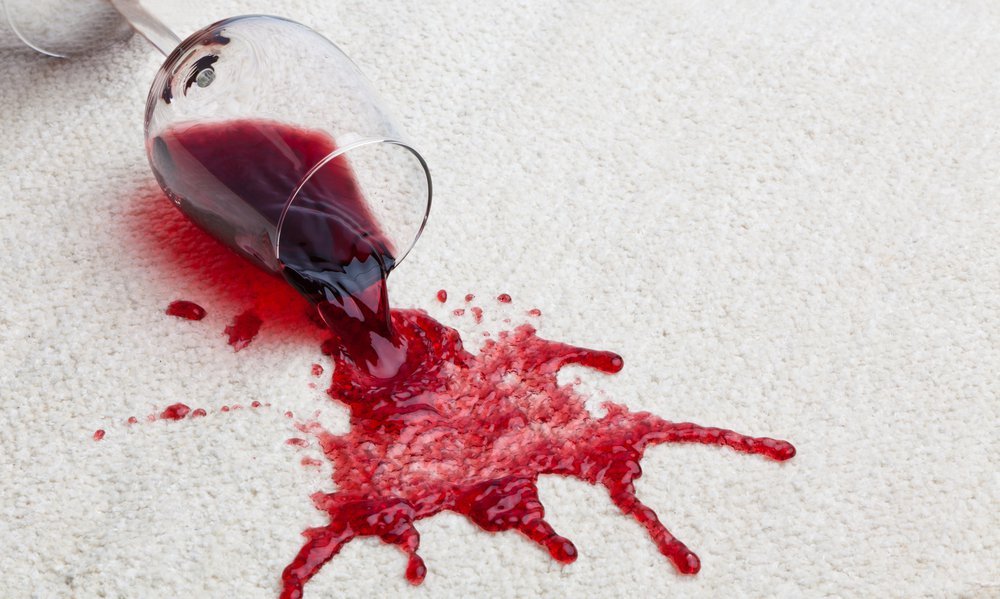 A toppled glass of red wine with a dirty carpet.