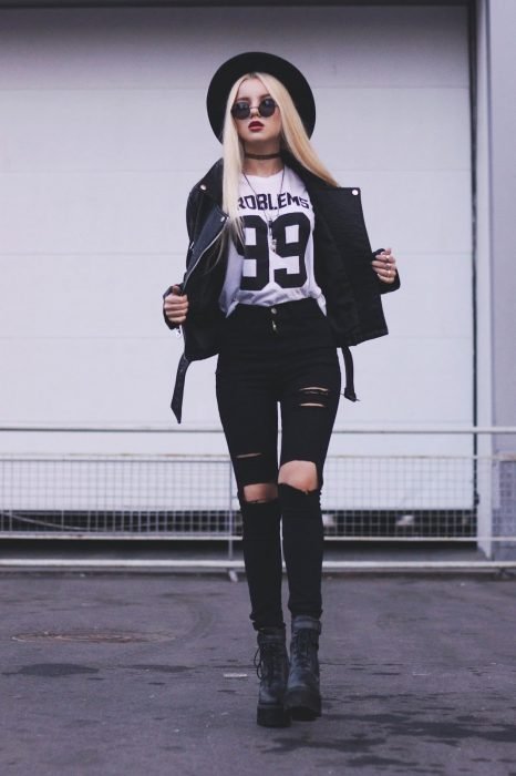 Chica modelando unos jeans negros rotos, camisa blanca con estampado, botas rockeras, sombrero bohemio y una chamarra de piel