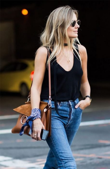 Chica caminando por la calle con jeans de mezclilla y top negro, con bolsa café y pulsera de pañuelo azul