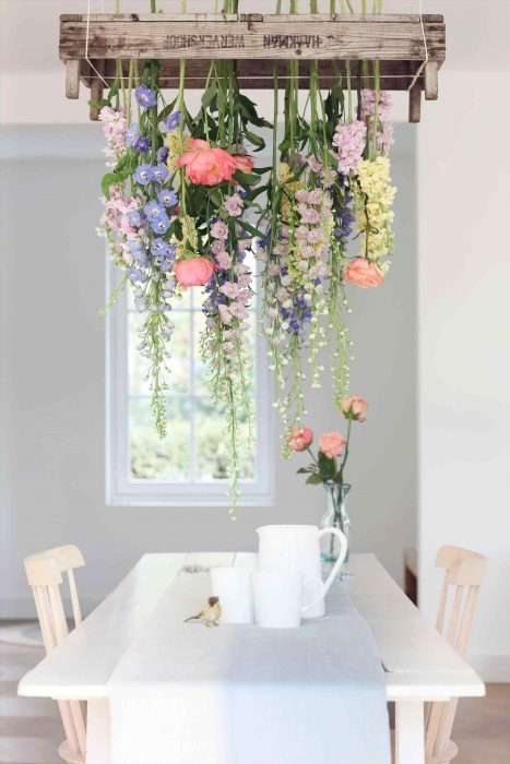 Comedor de una casa en colores neutros, decorada con una cascada de flores que cuelgan desde el techo hasta la mesa 
