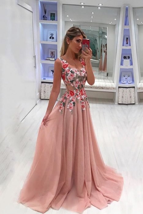 Chica tomándose una fotográfica con su celular, modelando un vestido rosa transparente con detalles de flores