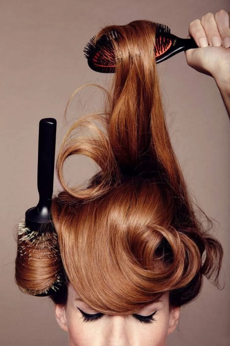 Mujer pelirroja peinándose el cabello con dos cepillos