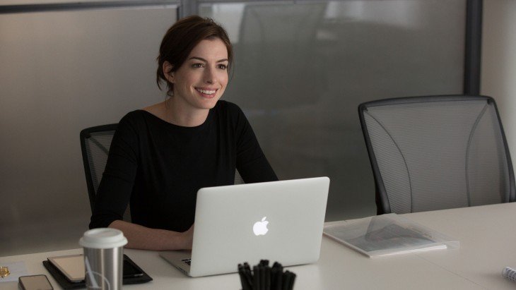 Actriz Anne Hathaway sentada sobre un escritorio frente a una laptop