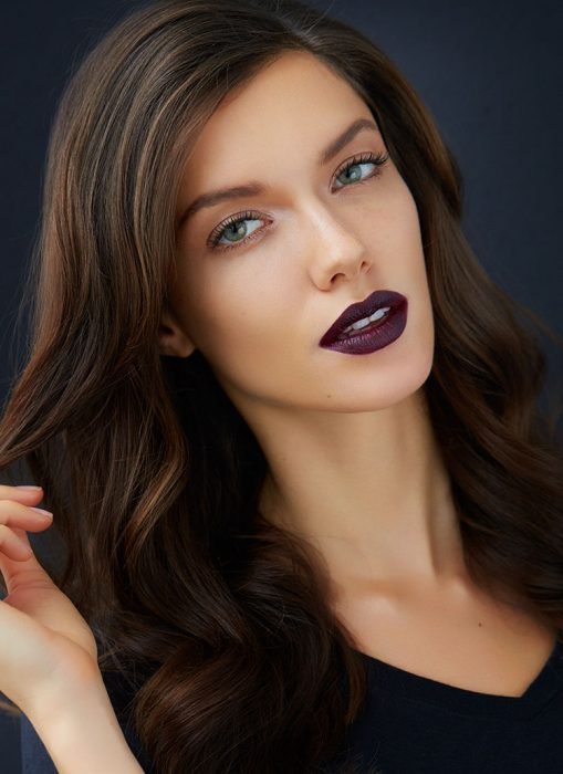 Chica usando un labial de color morado obscuro con un maquillaje ligero 