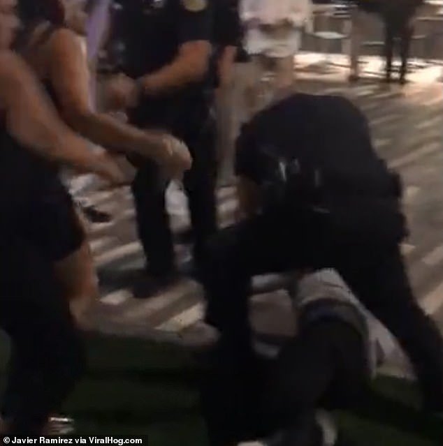 The woman can be seen lunging at the cop who is detaining her male associate on the ground