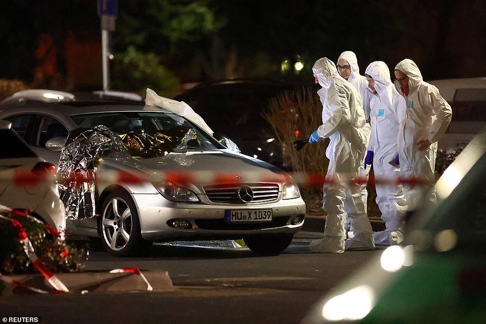 Forensic experts working around a damaged car that was covered emergency blankets and left with glass scattered around it after a shooting in Hanau