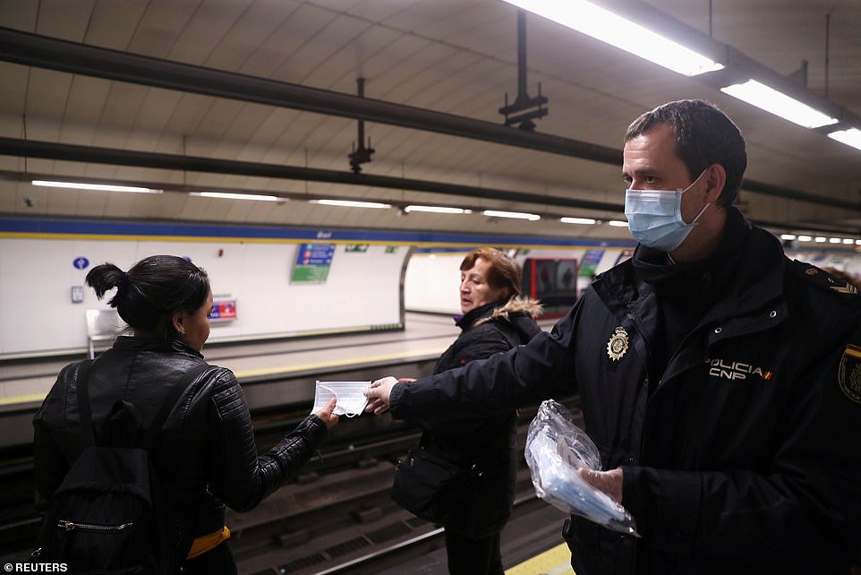 A police officer hands out a face mask - while also wearing one himself - at a Madrid metro station today as some workers were allowed to resume their jobs in Spain