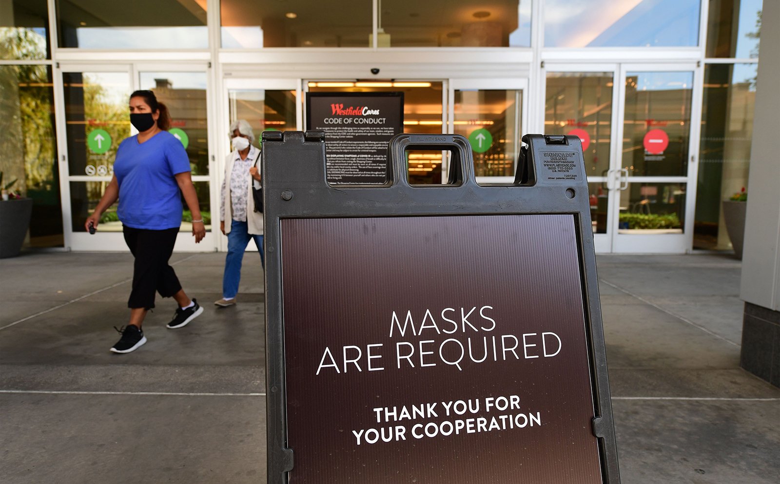 Women wearing face masks exit a shopping mall where a sign is posted at an entrance reminding people of the mask requirement Westfield Santa Anita shopping mall in Arcadia, California, on June 12.