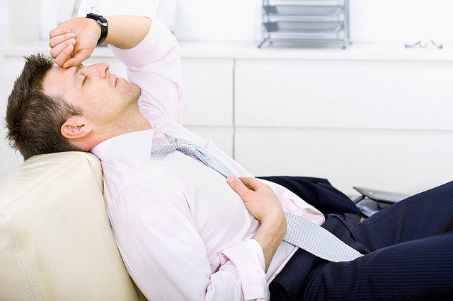 Mid-adult businessman lying on sofa at office, looking tired, eyes closed. Bright background.