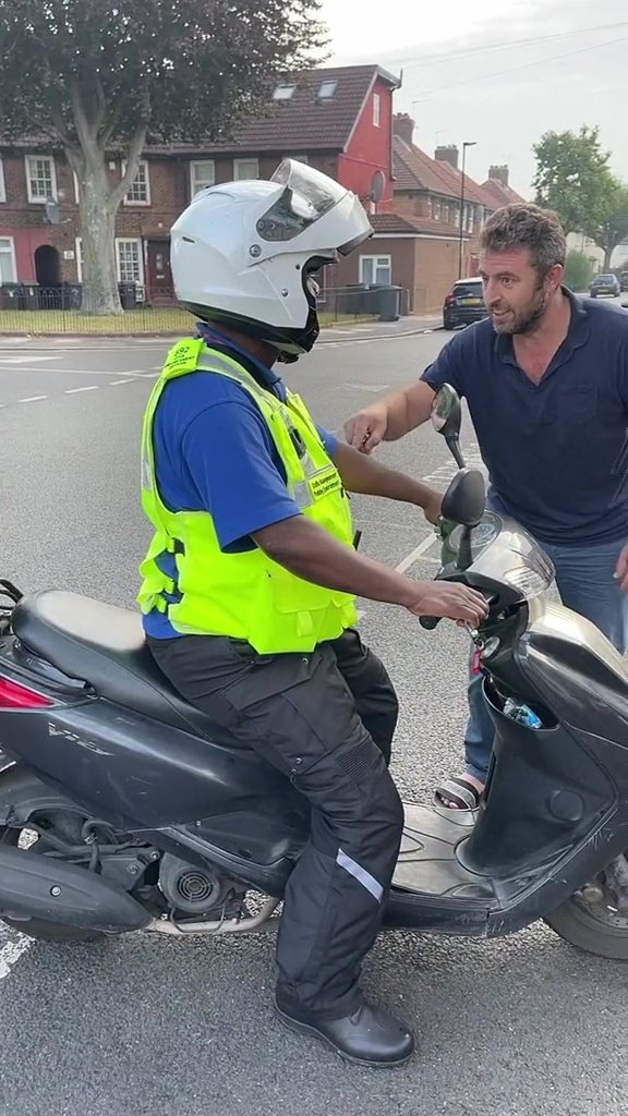 A man can be seen confronting a parking warden who sits on a scooter facing a row of homes