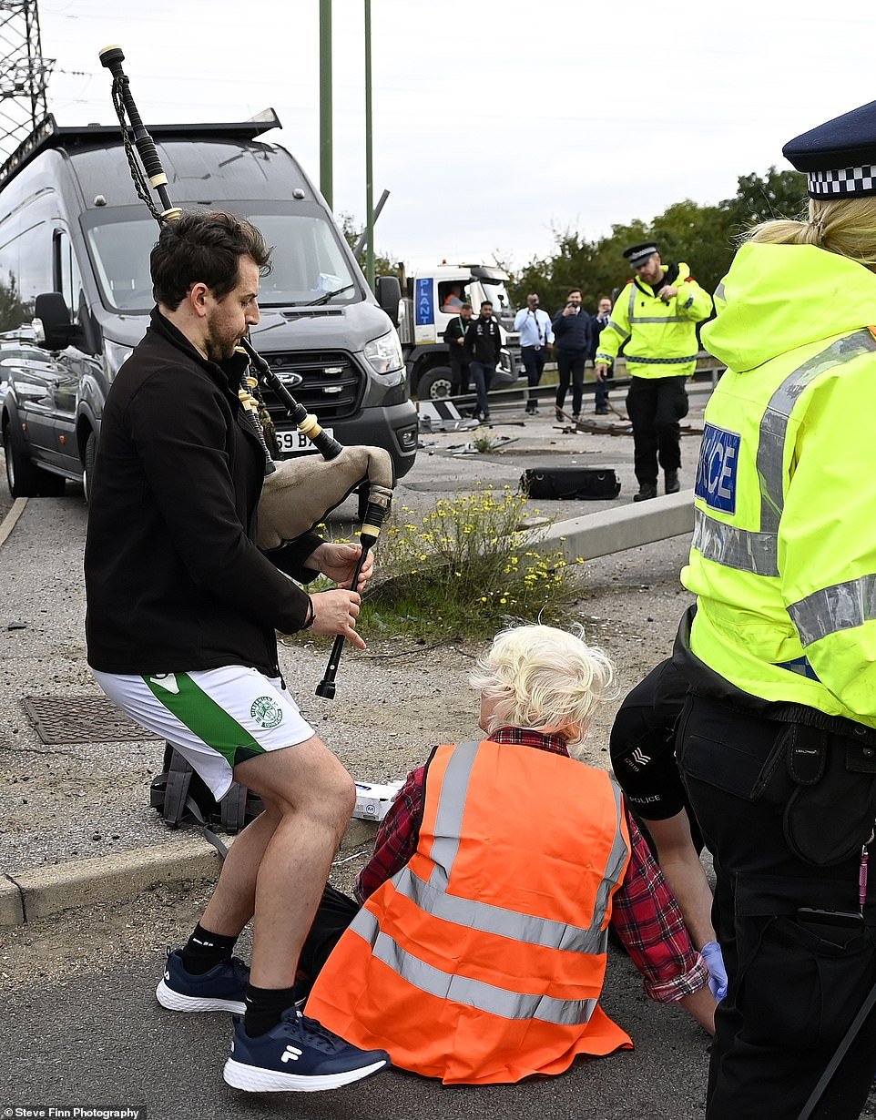 A man plays the bagpipes in the faces of Insulate Britain protesters sat on the road near the M25 Dartford Crossing today