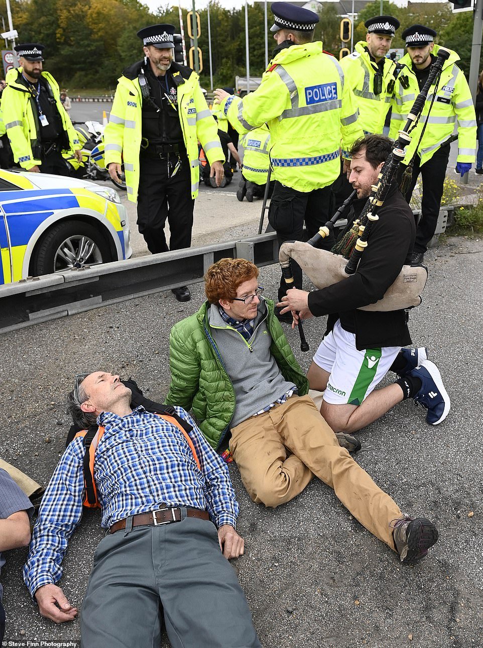 A man plays the bagpipes in the faces of Insulate Britain protesters sat on the road near the M25 Dartford Crossing today