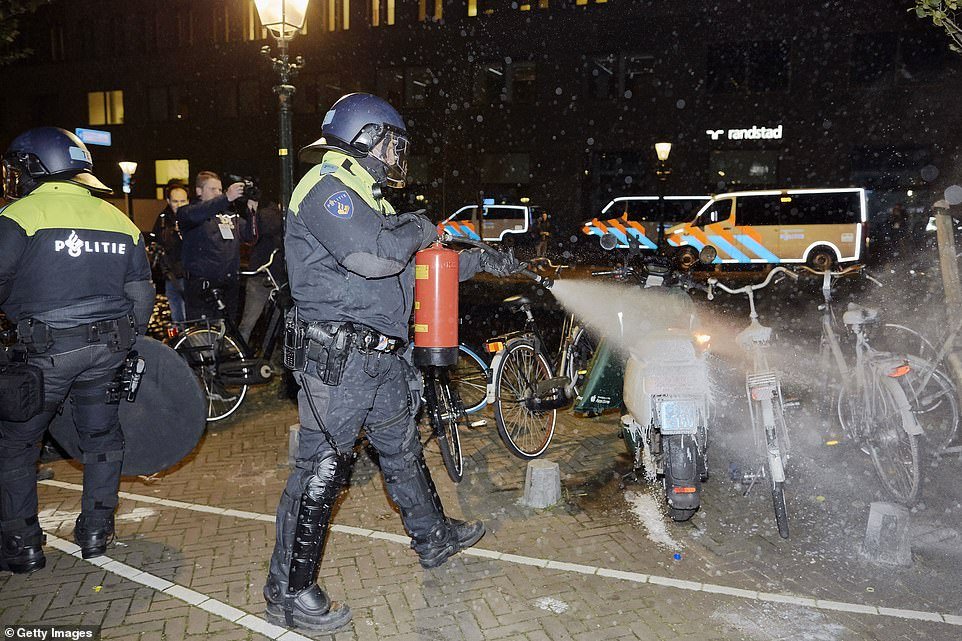 An anti-riot police officer extinguishes a burning scooter in The Hague, the Netherlands after protestors clashed with police