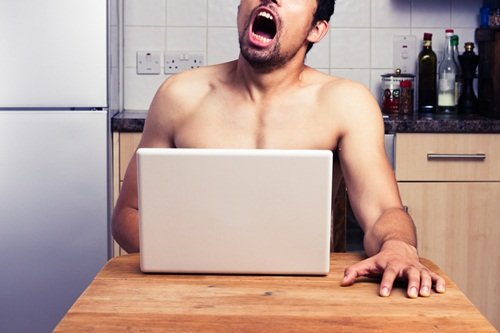 A naked man watching pornography in his kitchen